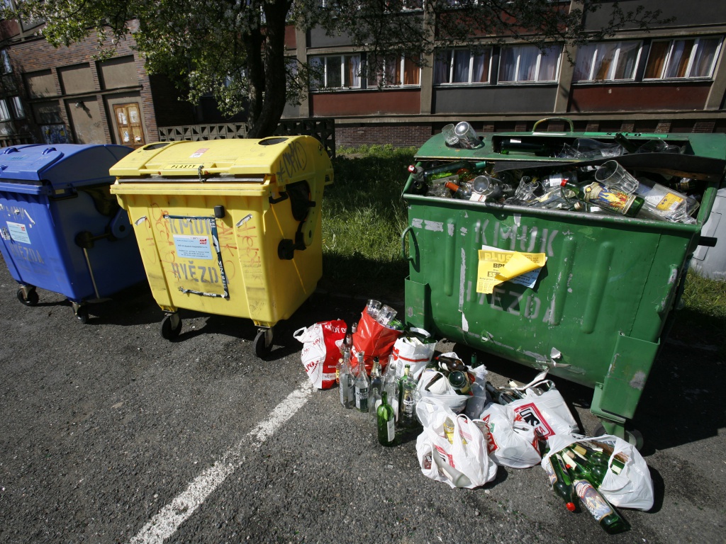 Přeplněný kontejner na sklo s taškami lahví vedle